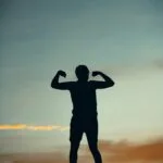 A powerful silhouette of a person flexing muscles against a vibrant sunset sky in India.
