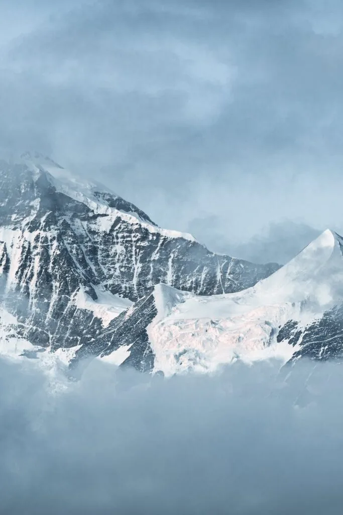 A serene view of snow-capped mountains surrounded by drifting clouds, offering a tranquil winter landscape.