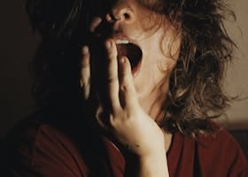 A woman with bed hair yawns in dim lighting, depicting fatigue and morning mood.