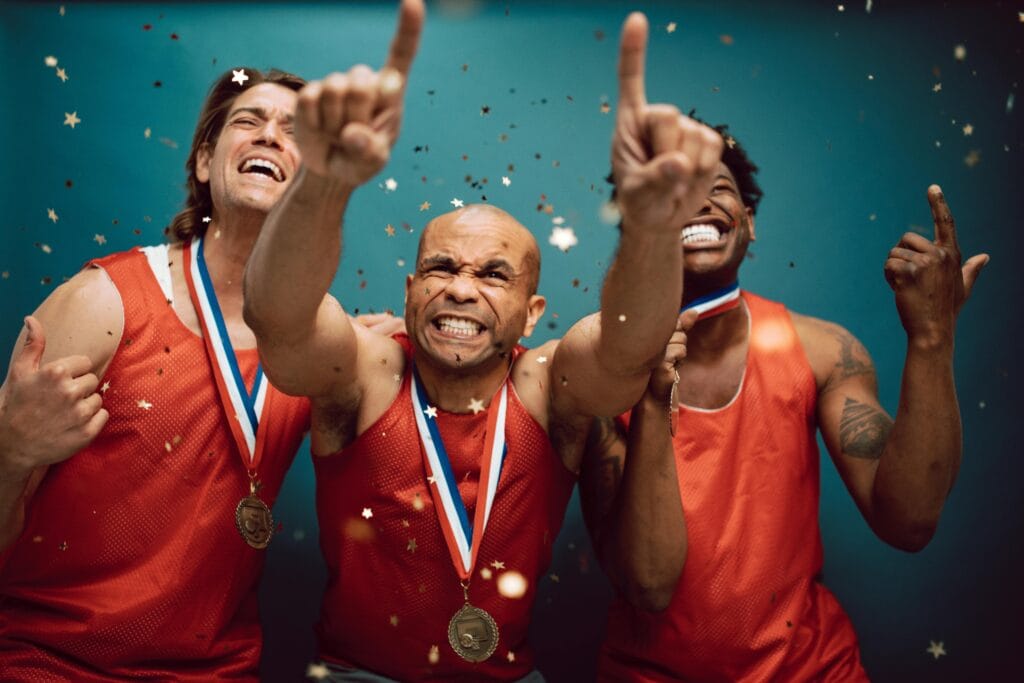 Three athletes celebrating victory with medals and confetti against a blue background.